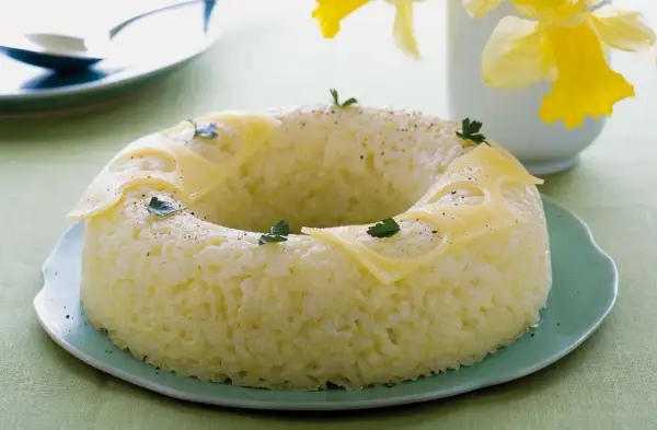 Sformato di riso a ciambella, decorato con fette di formaggio e prezzemolo, su un piatto verde.