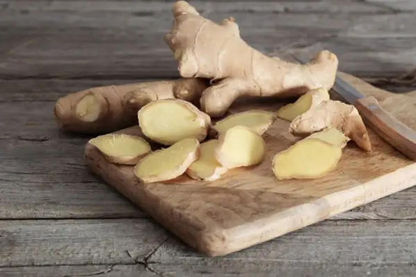 Frischer Ingwer, teils in Scheiben geschnitten, liegt auf einem Holzbrett. Der Unterschied zwischen ganzen Wurzeln und den Scheiben ist deutlich zu erkennen.