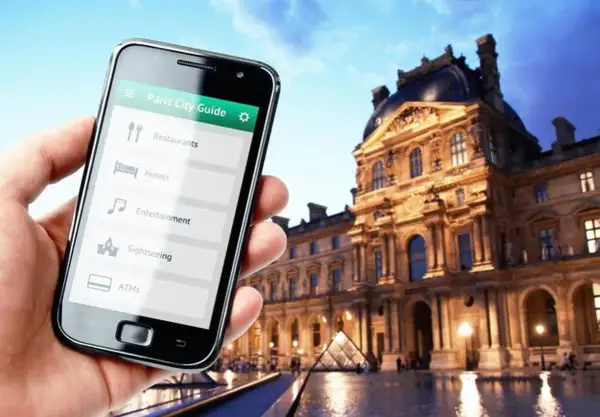 Smartfon z przewodnikiem po Paryżu w dłoni, w tle Luwr. Odkrywaj kody Francji!