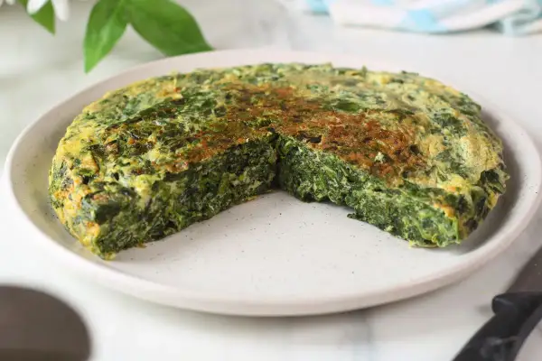 Frittata di spinaci dorata e soffice, tagliata a spicchi su un piatto bianco. Un piatto semplice e gustoso.