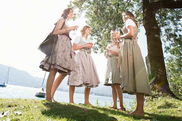 Vier Frauen in Dirndln stoßen am See an. Ein idyllisches Bild für Waldfeste in Bayern.