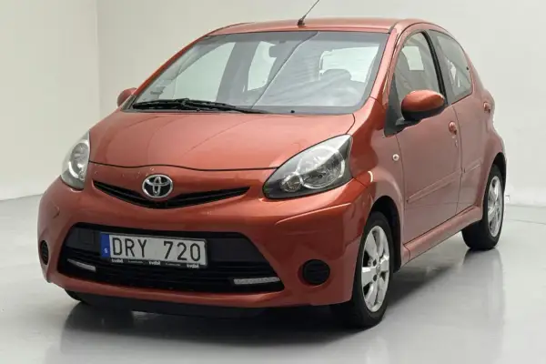 En orange Toyota Aygo med registreringsskylten DRY 720. Bilen verkar ha ett problem med fronten, kanske en buckla eller skada.