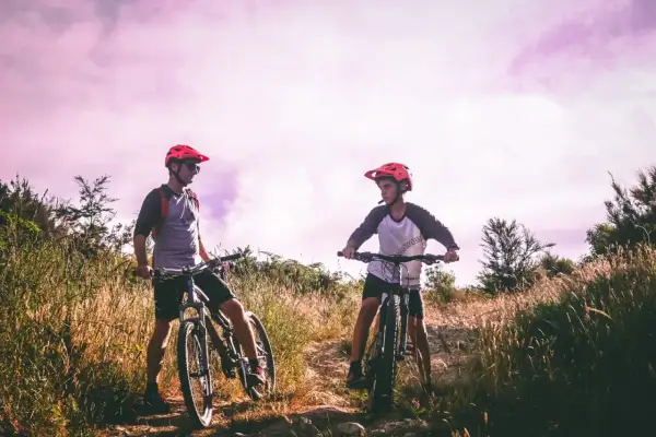 Dwóch rowerzystów w kaskach na tle fioletowego nieba, gotowych do jazdy po malowniczych trasach rowerowych Lublin.