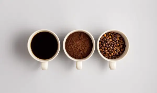Tre tazze mostrano il viaggio del caffè: chicchi tostati, macinato e bevanda scura. Un'idea di da dove proviene il caffè.