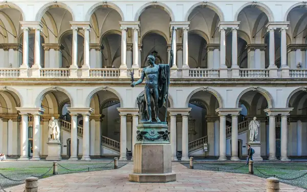 Dziedziniec Pinacoteca di Brera z rzeźbą w centrum i arkadowymi galeriami.