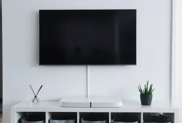 Minimalistyczny salon z telewizorem zamontowanym na ścianie. Pod nim biała szafka z ozdobami i schowkami. Idealna na jakiej wysokości telewizor.