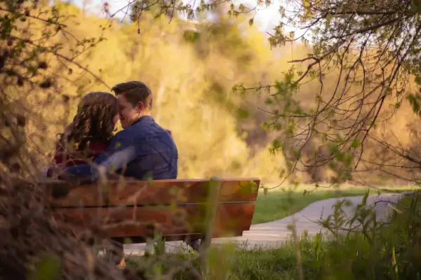Pareja abrazada en un banco, compartiendo un momento de amor verdadero entre la naturaleza.