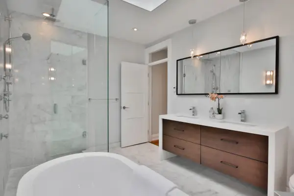 Bagno moderno con vasca freestanding, doccia in cristallo e mobile doppio lavabo con cassetti in legno. Le pareti sono rivestite in marmo, il soffitto è in cartongesso.