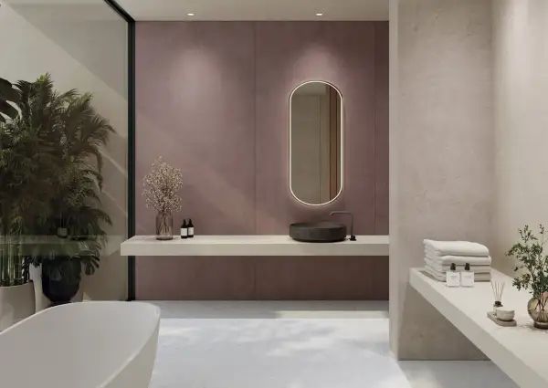 Elegante baño moderno con lavabo de piedra, espejo ovalado iluminado y azulejos de pared en tono malva. Toallas apiladas y plantas aportan calidez.