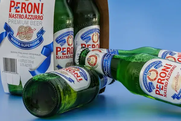Butelki piwa Peroni Nastro Azzurro leżą obok kartonu. Czy można trzymać alkohol w plastiku? Te butelki są szklane.
