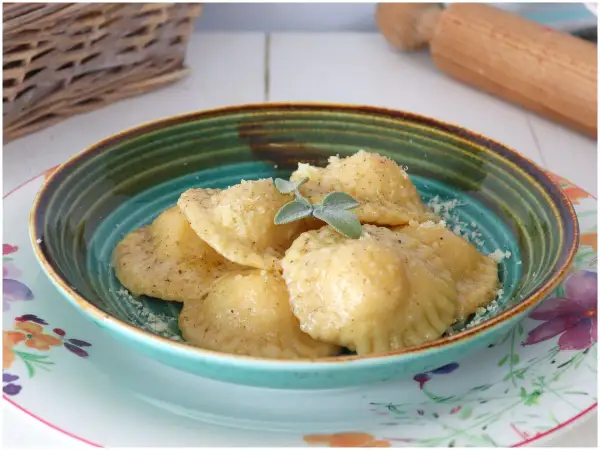 Tortelli di patate fumanti, cosparsi di parmigiano e guarniti con salvia, in una ciotola colorata.