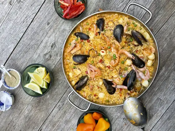 Ein köstliches Paella-Rezept mit Garnelen, Muscheln und Reis, garniert mit Zitronenspalten und Paprika.