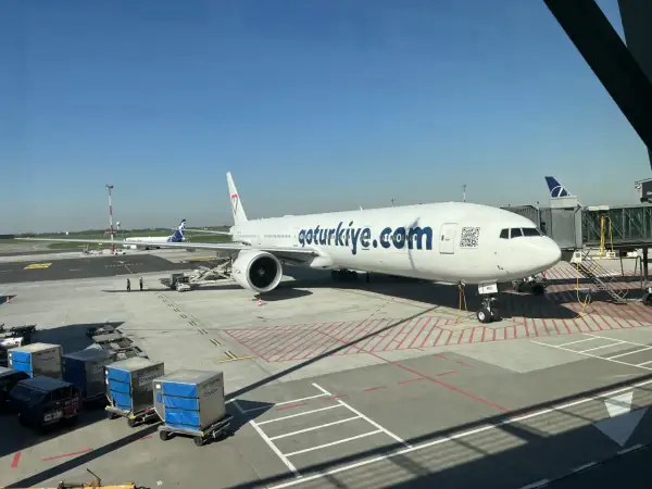 Samolot linii lotniczych MGA z napisem "goturkiye.com" na lotnisku. W tle widać inny samolot i rękaw.
