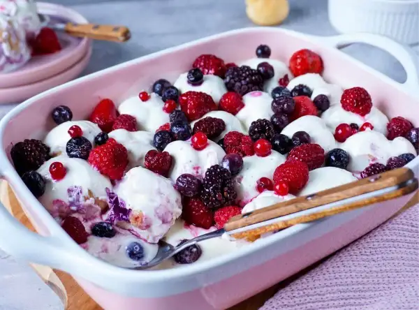 Ein cremiges Windbeutel-Dessert mit frischen Beeren wie Himbeeren, Blaubeeren und Brombeeren in einer rosa Schale.