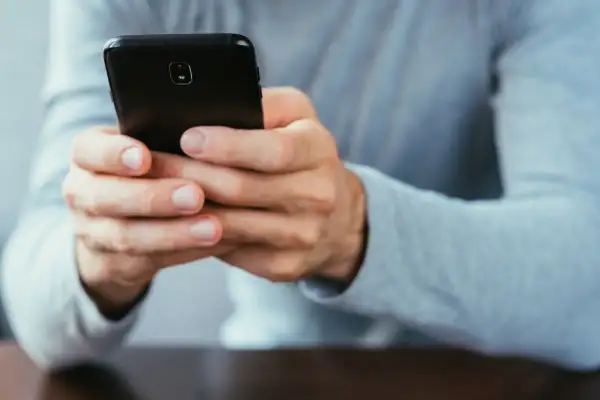 Dłonie trzymające czarny smartfon. Dowiedz się, jak się wylogować z FB na telefonie, by zadbać o prywatność.