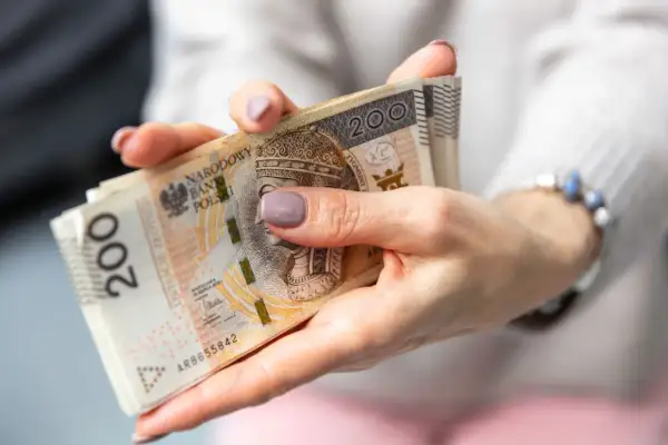 Dłonie trzymające stos banknotów 200 zł. Zastanawiasz się, jak wypłacić pieniądze z PPK?