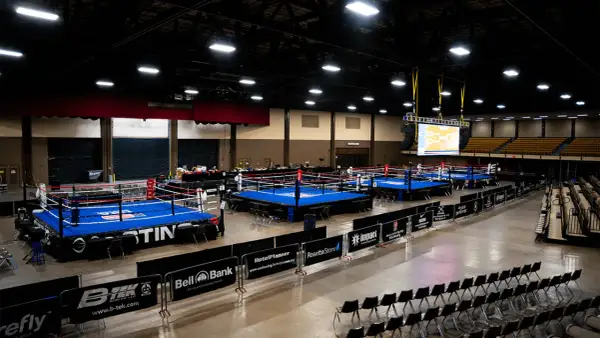 Multiple boxing rings are set up in an arena, ready for competition. A large screen displays a bracket, hinting at the usa boxing weight classes.