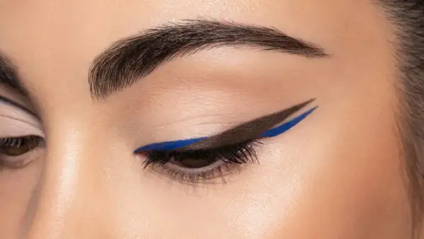 Occhio con eyeliner grafico marrone e blu elettrico, un audace cat crease che cattura lo sguardo.