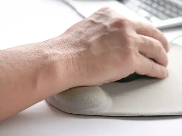 Dłoń na podkładce pod mysz, zapobiegającej syndromowi myszki komputerowej.