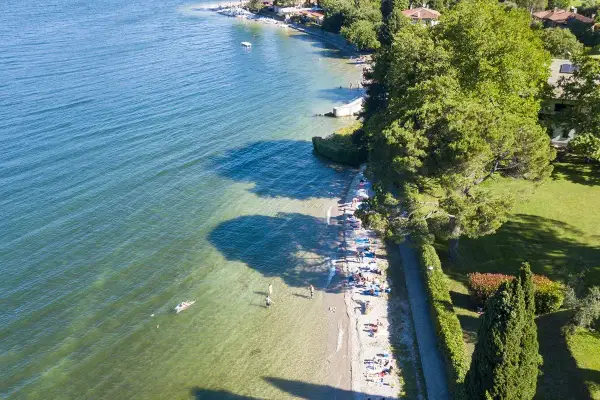 Słoneczny dzień nad jeziorem Como. Ludzie odpoczywają na plaży i pływają w krystalicznie czystej wodzie.