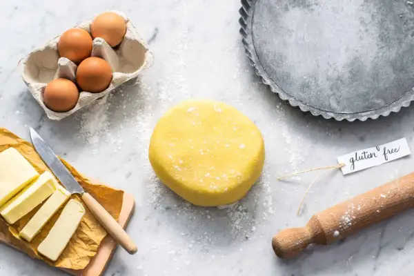 Impasto giallo per pasta frolla senza glutine, uova, burro e stampo per crostata pronti per creare un dolce delizioso.