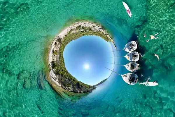 Rajskie **peloponez plaże** z krystalicznie czystą wodą, żaglówkami i ludźmi kąpiącymi się w słońcu.