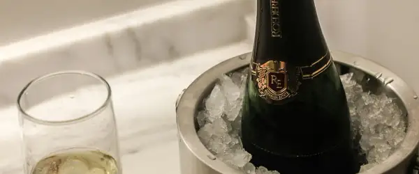 Eine Flasche Champagner in einem Eisbehälter, daneben ein Glas mit prickelndem Wein. Perfekt gekühlt, wann gefriert wein?