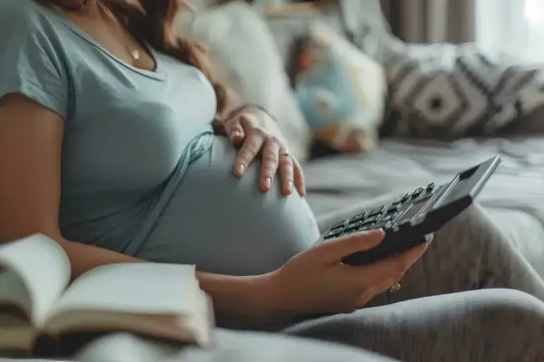 Ciężarna kobieta z kalkulatorem i otwartą książką na kanapie.