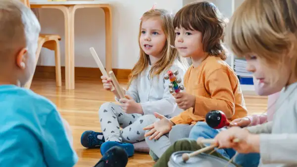 Kinder in der Kita lauschen gespannt einer Klanggeschichte und spielen mit Instrumenten.