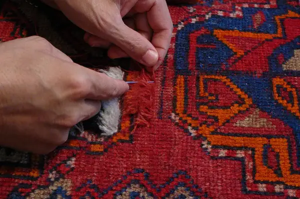 Mani che riparano un tappeto scolorito con ago e filo, un rimedio per ridare vita ai colori sbiaditi.