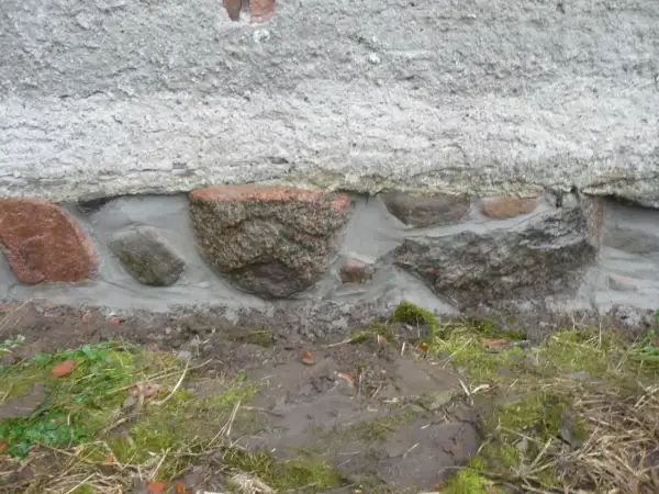Das Feldsteinfundament wird mit Mörtel abgedichtet. Große Steine sind sichtbar, umgeben von frischem Mörtel, der die Lücken füllt.