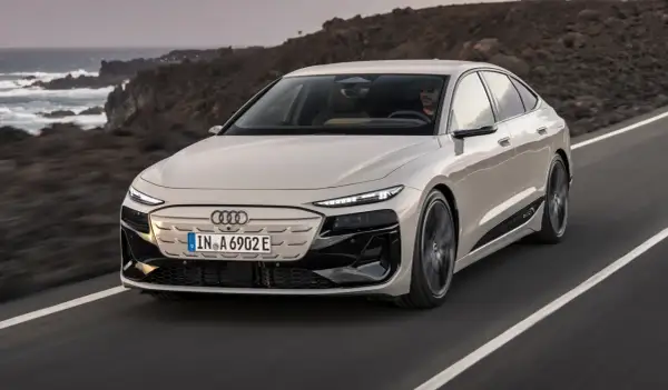 Elegancki Audi A6 e-tron w kolorze jasnego beżu przemierza malowniczą, skalistą trasę nad oceanem.