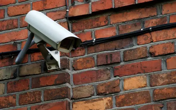 Caméra de surveillance blanche fixée sur un mur de briques. Comment reconnaître une caméra factice ? Cherchez l'absence de câbles ou de voyants lumineux.
