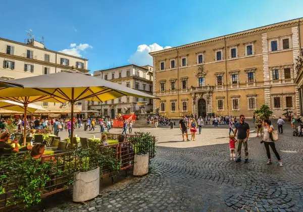 Piazza animata con persone che passeggiano e si godono un caffè all'aperto, un assaggio delle serate Erasmus a Roma.