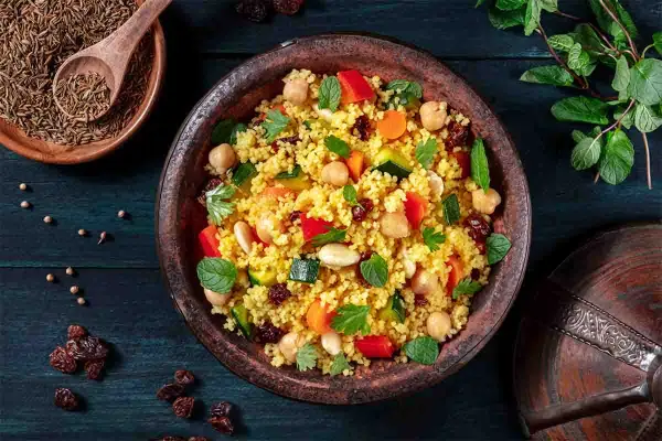 Un piatto colorato di cous cous, con ceci, verdure e uvetta, che evoca le sue antiche origini.