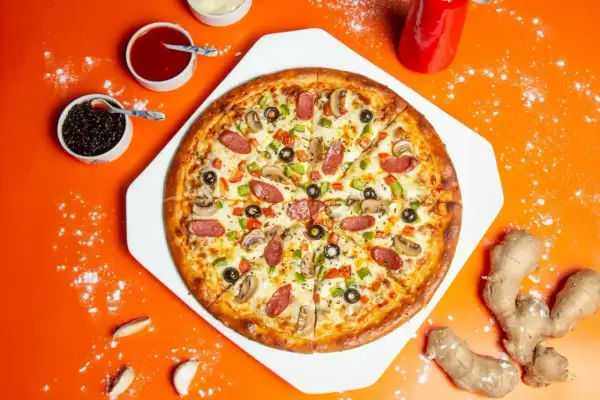 Pyszna pizza z kiełbasą, pieczarkami i oliwkami. Obok sosy, czosnek i imbir – idealne składniki na pizzę.