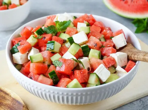 Erfrischender Melonensalat mit Mozzarella, Gurken und Minze in einer weißen Schüssel. Perfekt für heiße Tage!
