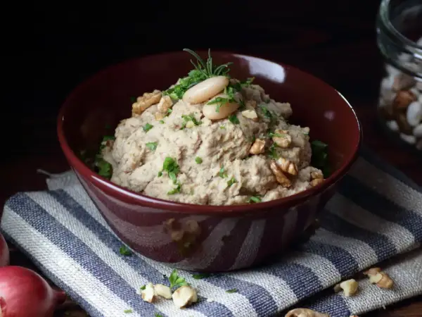 Aksamitna pasta z lubczyku, udekorowana fasolką, orzechami i ziołami, w bordowej misce na pasiastym obrusie.