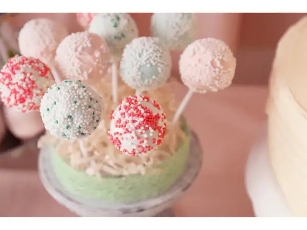 Bunte Kuchen am Stiel, verziert mit Perlen und Streuseln, auf einem grünen Podest arrangiert.