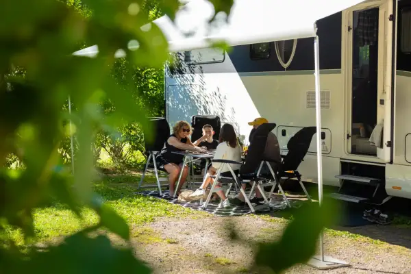 Family playing cards at a table outside a camper van on a sunny day.