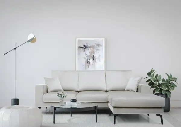 Divano angolare color crema, con tavolino rotondo in vetro, pouf bianco e quadro astratto. Le misure divano angolare sono perfette per questo spazio.