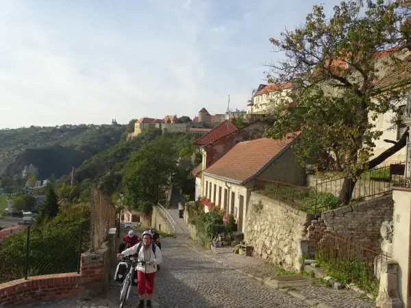 Radfahrer erkunden eine Kopfsteinpflasterstraße in Znaim, Tschechien, mit historischen Gebäuden und einer Burgruine im Hintergrund.