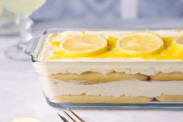 Ein erfrischendes Zitronen Tiramisu in einer Glasform, garniert mit Zitronenscheiben und einem Hauch von Zitronensauce.