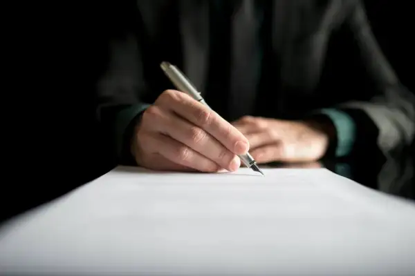 Dłoń pisze piórem na dokumencie. Może to być dziennik budowy, przerwa we wpisach lub ważny kontrakt.