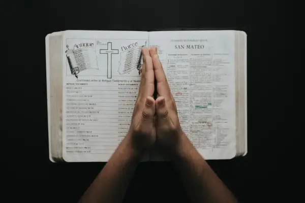 Dłonie złożone do modlitwy na otwartej Biblii. To inspiracja na modlitwa na każdy dzień tygodnia.