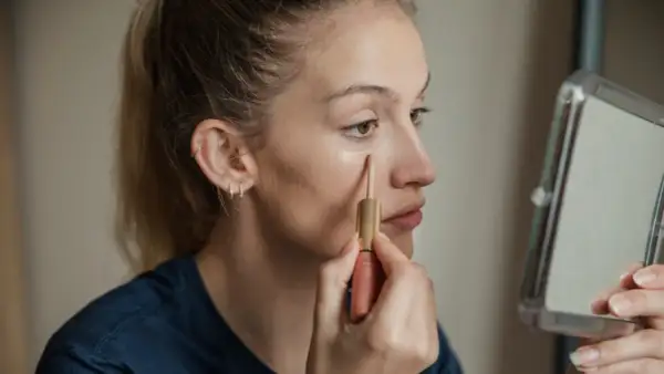 Ragazza applica correttore sotto l'occhio, un passo per capire il colore del correttore online.