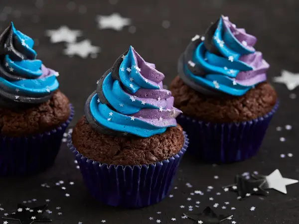 Drei Schoko-Cupcakes mit blau-lila Sternen-Frosting, inspiriert von einem Galaxie-Cupcake-Rezept.