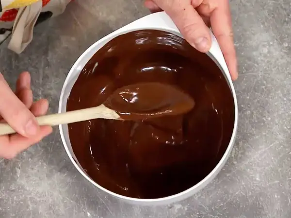 En sked rör i en skål med glansig choklad. Perfekt för ett enkelt ganache recept.