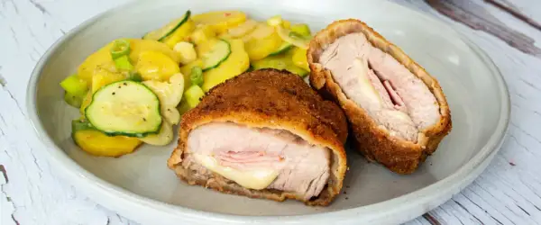 Zwei goldbraune Cordon Bleu, gefüllt mit Schinken und Käse, daneben ein bunter Kartoffel-Zucchini-Salat. Ein leckeres Cordon Bleu Rezept!