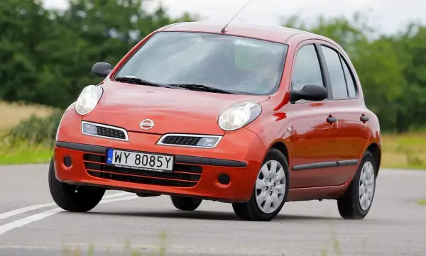 Pomarańczowy Nissan Micra K12 na drodze, z zielenią w tle.